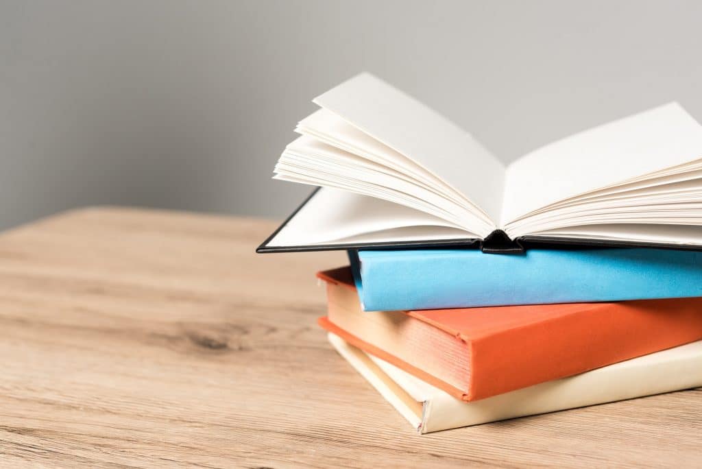 stack of books and open blank notebook on wooden desk on grey background